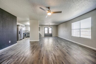 Unfurnished living room with ceiling fan with notable chandelier, a textured ceiling, and dark wood-type flooring