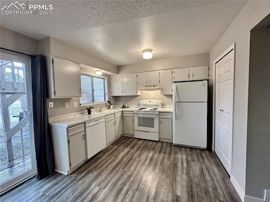 Kitchen with white appliances, light countertops, dark wood-style flooring, a textured ceiling, and under cabinet range hood