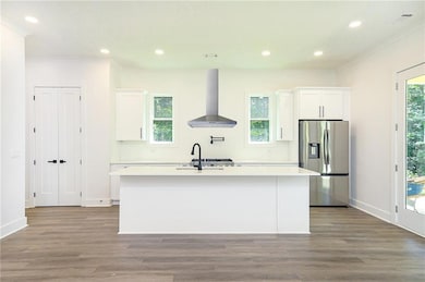 Kitchen with wall chimney range hood, stainless steel fridge with ice dispenser, a center island with sink, white cabinetry, and crown molding