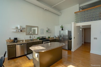 Kitchen with stainless steel appliances, light stone counters, light wood finished floors, a center island, and a towering ceiling