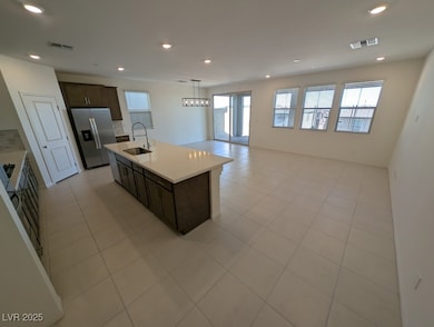 Kitchen featuring dark brown cabinetry, recessed lighting, open floor plan, stainless steel refrigerator with ice dispenser, and hanging light fixtures