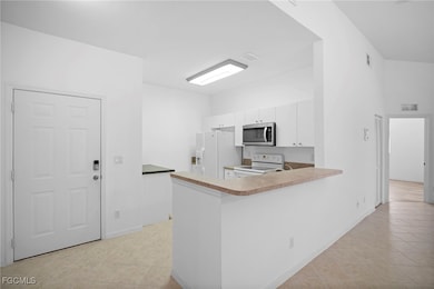 Kitchen with light tile patterned flooring, a peninsula, white appliances, white cabinetry, and light countertops