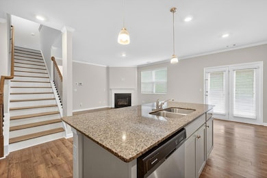 Kitchen featuring crown molding, stainless steel dishwasher, wood finished floors, pendant lighting, and a glass covered fireplace