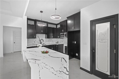 Kitchen featuring dark cabinets, marble finish floor, backsplash, light stone countertops, and stainless steel microwave