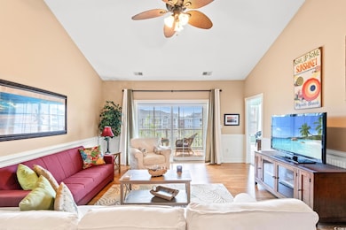 Living room with a wainscoted wall, light wood finished floors, a ceiling fan, and vaulted ceiling