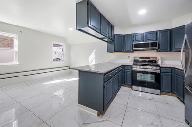 Kitchen featuring backsplash, light marble finish flooring, appliances with stainless steel finishes, light stone countertops, and a peninsula