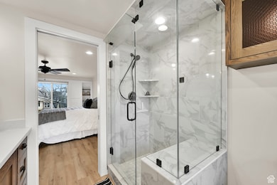 Full bath with connected bathroom, a marble finish shower, light wood finished floors, vanity, and a ceiling fan