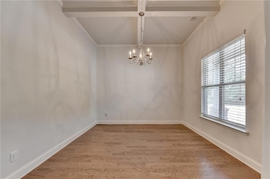 Empty room with beamed ceiling, crown molding, light wood finished floors, a chandelier, and coffered ceiling