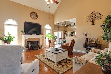 Living area with high vaulted ceiling, wood-type flooring, a fireplace with flush hearth, and a ceiling fan