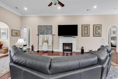 Living area with arched walkways, a ceiling fan, crown molding, a lit fireplace, and recessed lighting