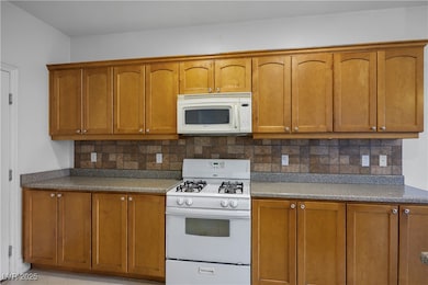 Kitchen with white appliances, brown cabinetry, and decorative backsplash