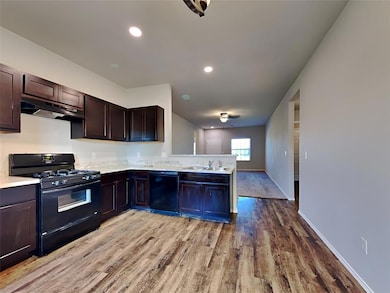 Kitchen featuring black appliances, under cabinet range hood, light wood-style floors, a peninsula, and light countertops