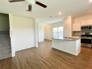 Kitchen with appliances with stainless steel finishes, dark wood finished floors, white cabinetry, a center island with sink, and recessed lighting