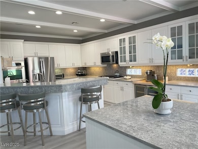 Kitchen featuring white cabinets, tasteful backsplash, stainless steel appliances, glass insert cabinets, and beamed ceiling
