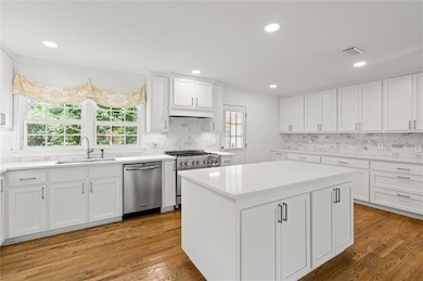 Kitchen with appliances with stainless steel finishes, a sink, tasteful backsplash, light countertops, and white cabinetry