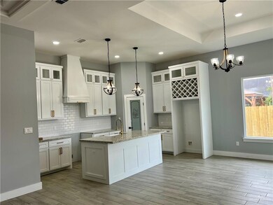 Kitchen with a center island with sink, custom exhaust hood, tasteful backsplash, and white cabinetry