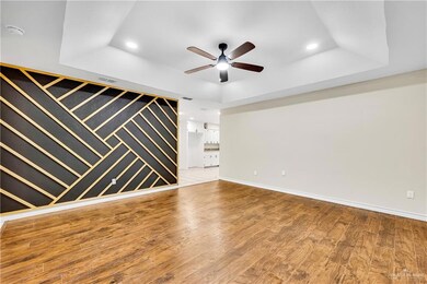 Unfurnished living room featuring a raised ceiling, recessed lighting, a ceiling fan, wood finished floors, and baseboards
