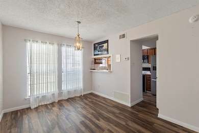 Unfurnished dining area with dark wood-style flooring, a textured ceiling, and a chandelier