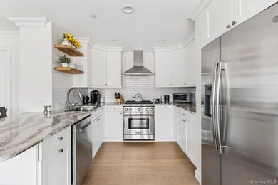 Kitchen with appliances with stainless steel finishes, decorative backsplash, open shelves, light stone counters, and light wood finished floors