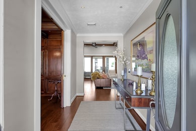 This elegant entryway welcomes you with beautiful hardwood floors, soft neutral tones, and detailed crown molding. The open layout provides a clear view into the inviting living area, showcasing the home’s warm and sophisticated design. A stylish console and decorative accents create an immediate sense of charm and refinement.