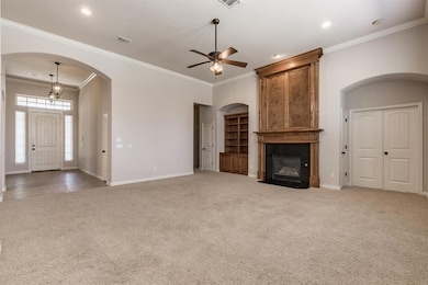 Unfurnished living room featuring light carpet, baseboards, a tiled fireplace, a ceiling fan, and arched walkways
