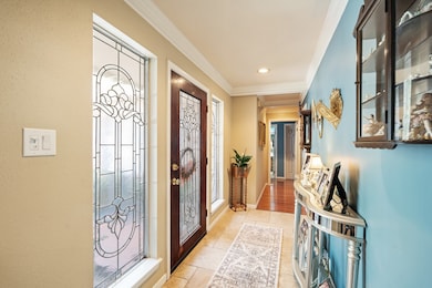 This photo captures a warm and elegant entryway that blends classic charm with inviting character. The focal point is the beautiful front door, crafted from rich wood and adorned with intricate decorative glass panels that also appear on the matching sidelights, allowing soft, diffused natural light to brighten the hallway.