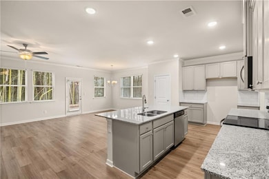Kitchen featuring gray cabinets, crown molding, an island with sink, a chandelier, and tasteful backsplash