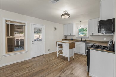 Kitchen featuring white cabinets, black microwave, range with gas cooktop, light wood-style floors, and hanging light​​‌​​​​‌​​‌‌​​‌​​​‌‌​​​​​​‌‌‌​​‌​​‌‌​​​‌ fixtures