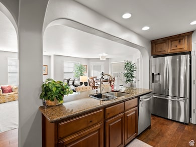Kitchen featuring arched walkways, dark wood-type flooring, dark stone counters, stainless steel appliances, and open floor plan