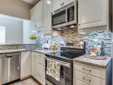Kitchen featuring appliances with stainless steel finishes, tasteful backsplash, white cabinetry, and light stone counters
