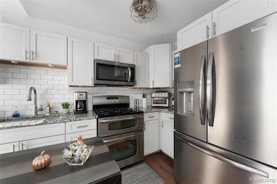 Kitchen with appliances with stainless steel finishes, light stone countertops, white cabinets, backsplash, and dark wood-style floors
