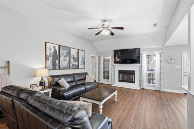 Living area with a fireplace with raised hearth, wood finished floors, vaulted ceiling, and ceiling fan