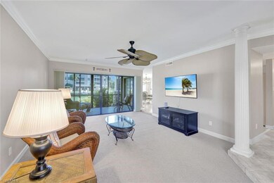 Carpeted living room featuring ornate columns, ceiling fan, and crown molding