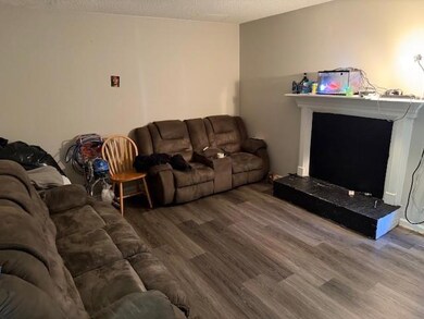 Living area with wood finished floors, a textured ceiling, and a fireplace with raised hearth