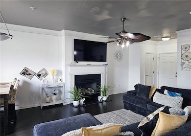 Living room featuring wood finished floors, a ceiling fan, baseboards, ornamental molding, and a fireplace