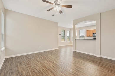 Unfurnished living room with wood finished floors, arched walkways, and ceiling fan
