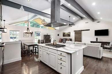 Kitchen featuring dark hardwood / wood-style flooring, stainless steel gas stovetop, a barn door, beam ceiling, and island range hood