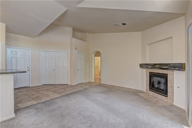 Unfurnished living room with light colored carpet, arched walkways, a tiled fireplace, light tile patterned floors, and high vaulted ceiling