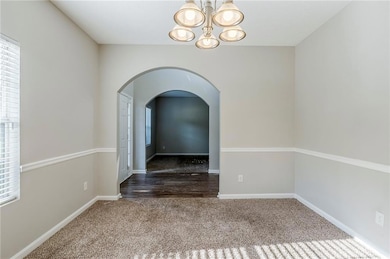 Empty room with carpet, a chandelier, arched walkways, and baseboards