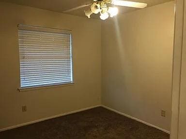 Spare room featuring baseboards, dark carpet, and 