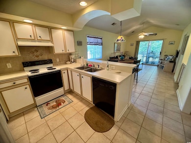 Kitchen featuring electric range oven, black dishwasher, a sink, under cabinet range hood, and a peninsula