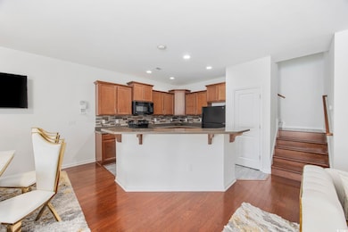 Kitchen featuring a center island, a kitchen breakfast bar, dark hardwood / wood-style flooring, decorative backsplash, and black appliances