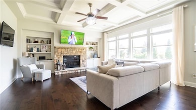 Living area with baseboards, a stone fireplace, a ceiling fan, dark wood-style floors, and beamed ceiling