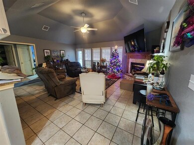Tiled living room with ceiling fan, a brick fireplace, and a raised ceiling
