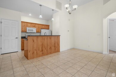 Kitchen with hanging light fixtures, white appliances, light tile patterned flooring, a chandelier, and a towering ceiling