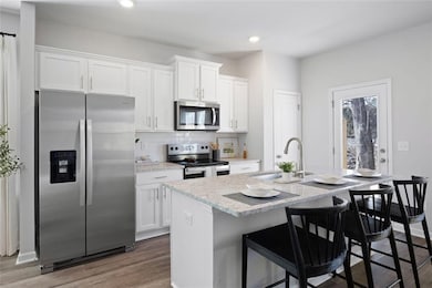 Kitchen with a sink, a center island with sink, white cabinets, and appliances with stainless steel finishes