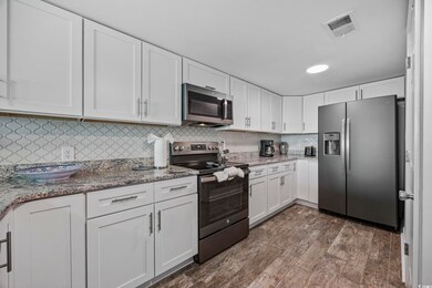 Kitchen featuring appliances with stainless steel finishes, white cabinets, decorative backsplash, light stone counters, and dark wood-type flooring