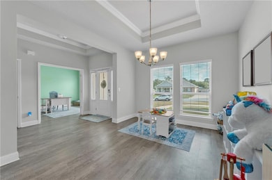 Dining space with wood finished floors, a chandelier, crown molding, a tray ceiling, and baseboards