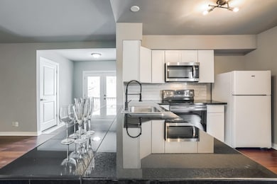 Kitchen with dark wood-type flooring, stainless steel appliances, white cabinets, french doors, and decorative backsplash