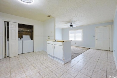 Kitchen with a textured ceiling, light tile patterned flooring, light countertops, white cabinetry, and ornamental molding